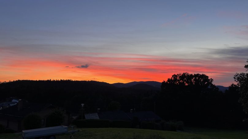 Abendrot Farbige Abenddämmerung über silhouettenhaften Bergen und Bäumen.