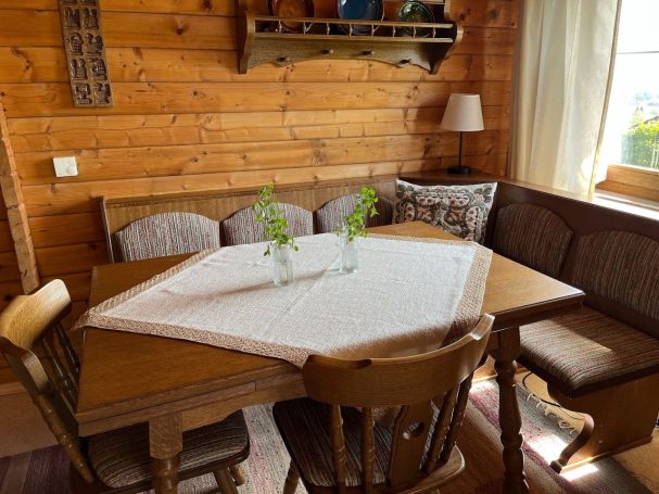 Tisch mit Eckbank Holztisch in gemütlicher Stube, dekoriert mit einer Tischdecke und Pflanzen in Vasen.